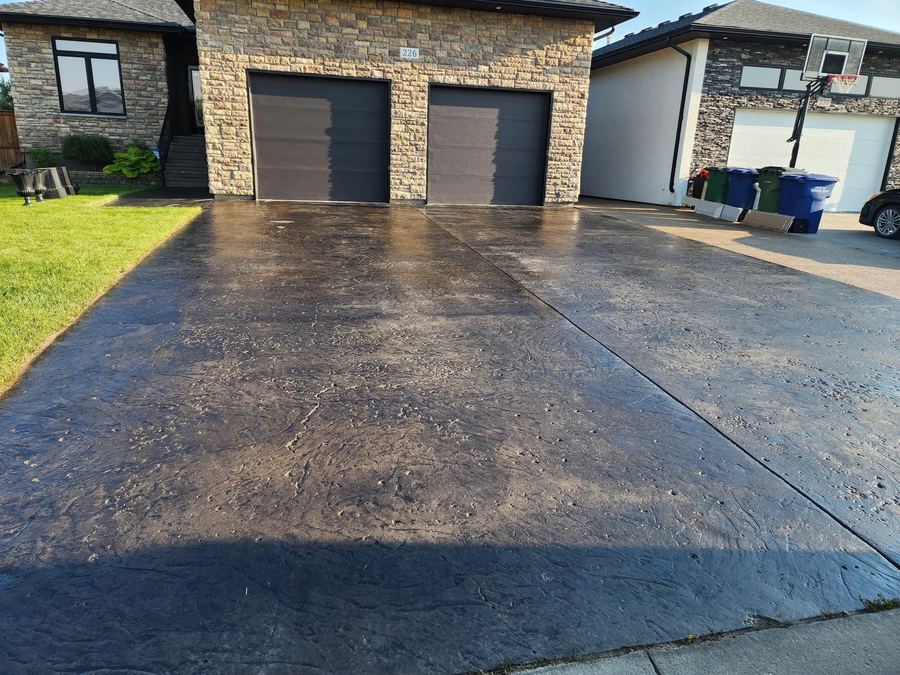 Dark sealed stamped concrete driveway leading to a stone-faced double garage