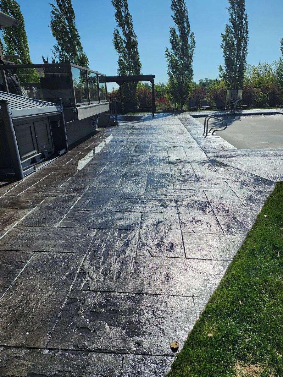Sealed stamped concrete walkway with a wet-look finish beside a backyard fence