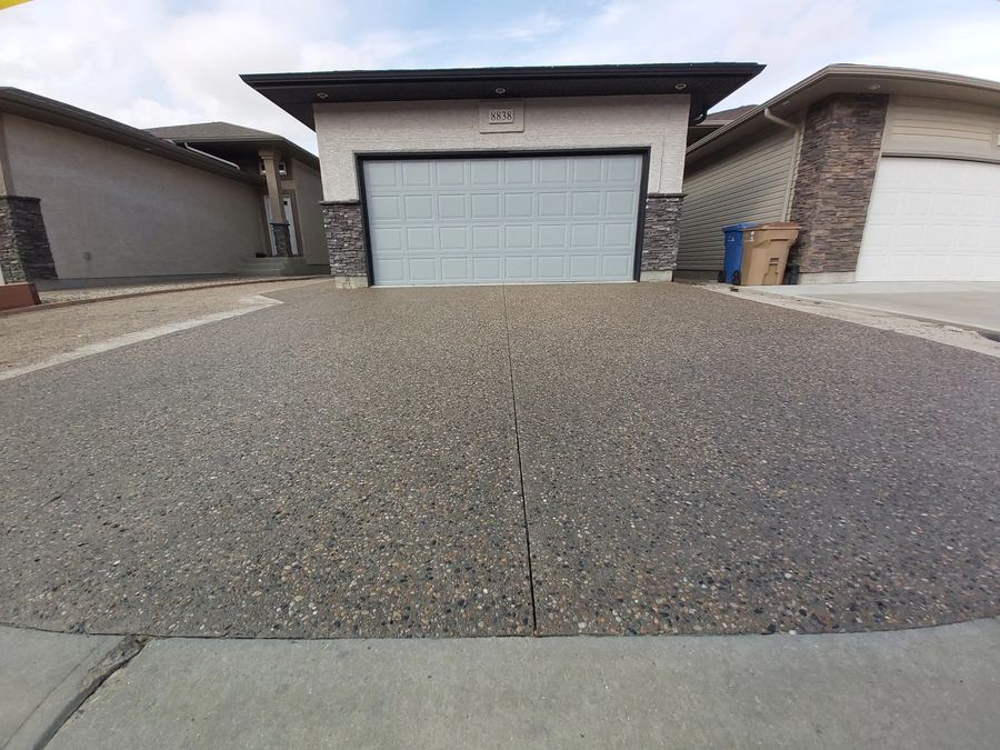 Exposed aggregate driveway cleaned and sealed in front of a white garage door