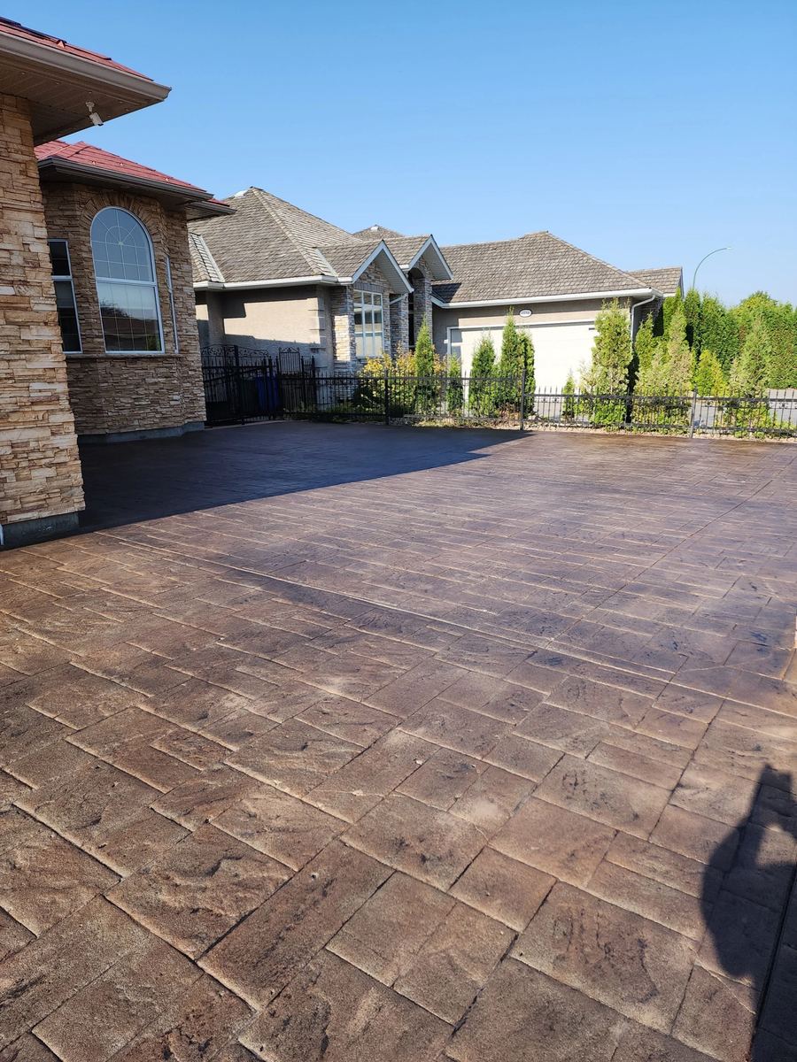 Warm-toned sealed stamped concrete driveway alongside a landscaped yard